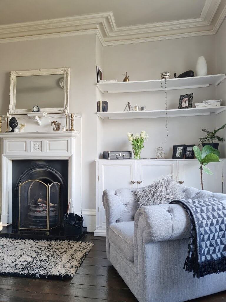 Victorian living room painted in soft greys with original fireplace, alcove shelves and grey Chesterfield style chair. 