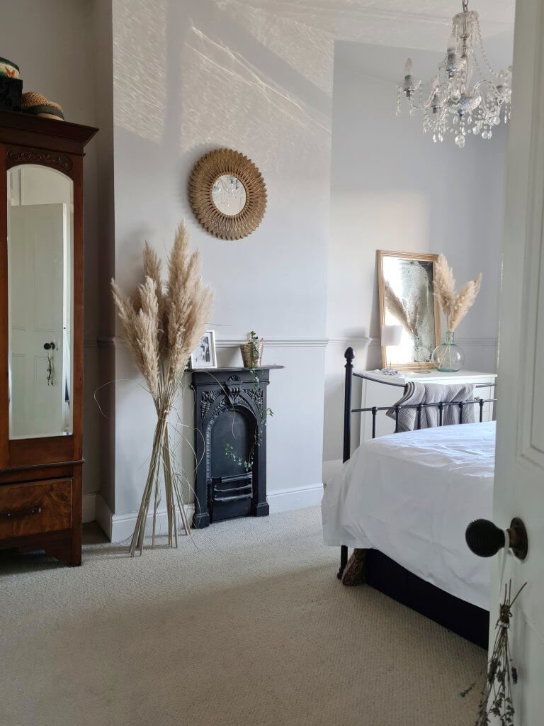 Master bedroom in a Victorian terrace with black fireplace, antique wardrobe and chest of drawers. Large pampas grass to the side of the fireplace. From a blog post about neutral paint colours in period homes by Life with Holly