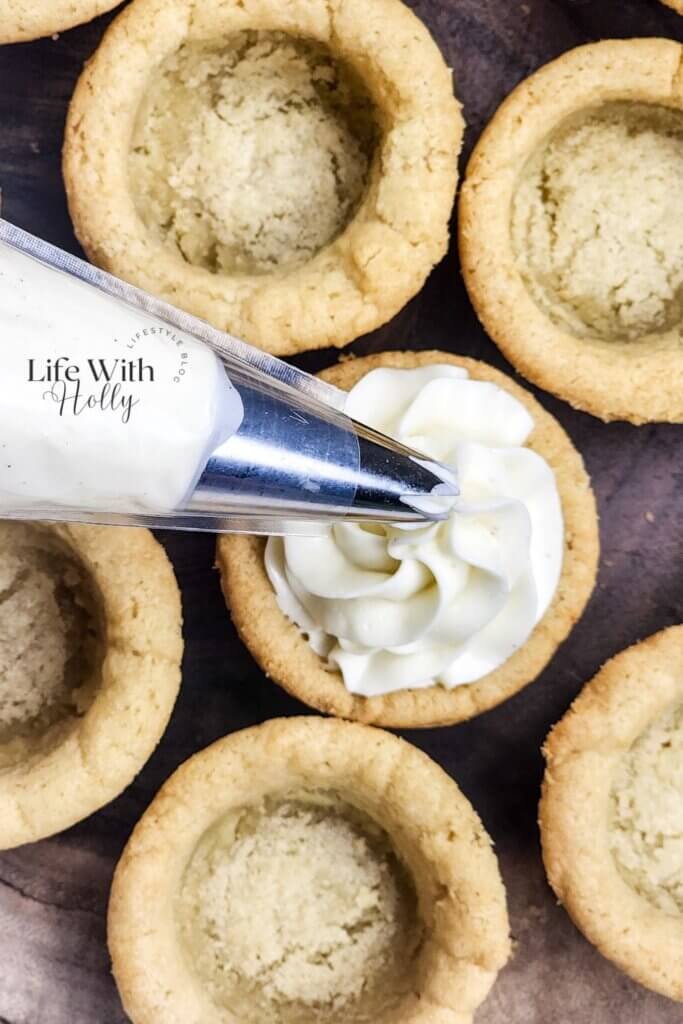 Piping cheesecake filling into strawberry cheesecake cookie cups